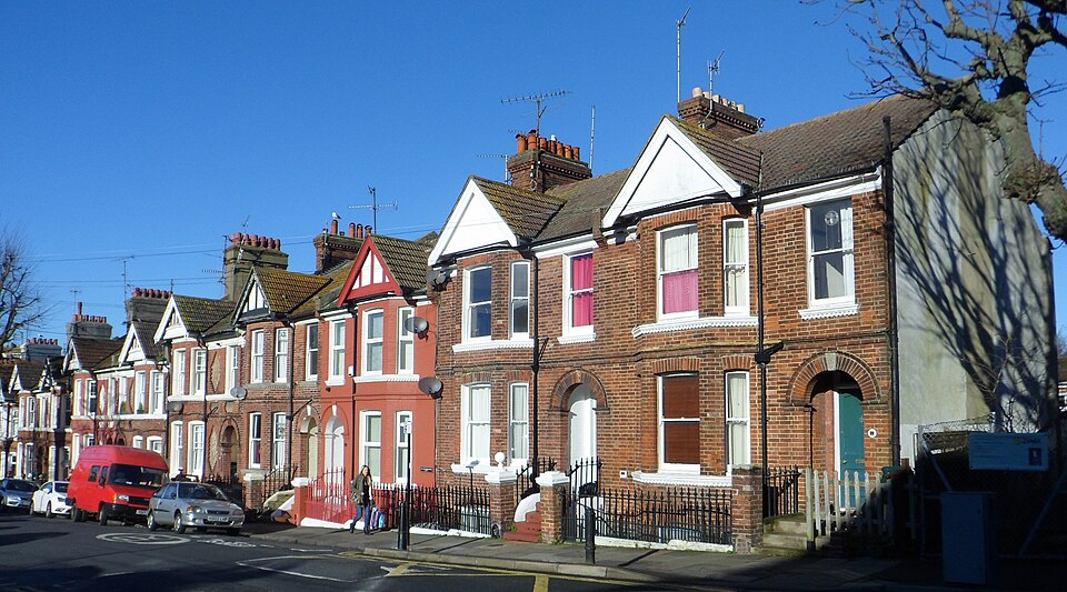 A row of red-brick Victorian terraced houses with bay windows under a blue sky